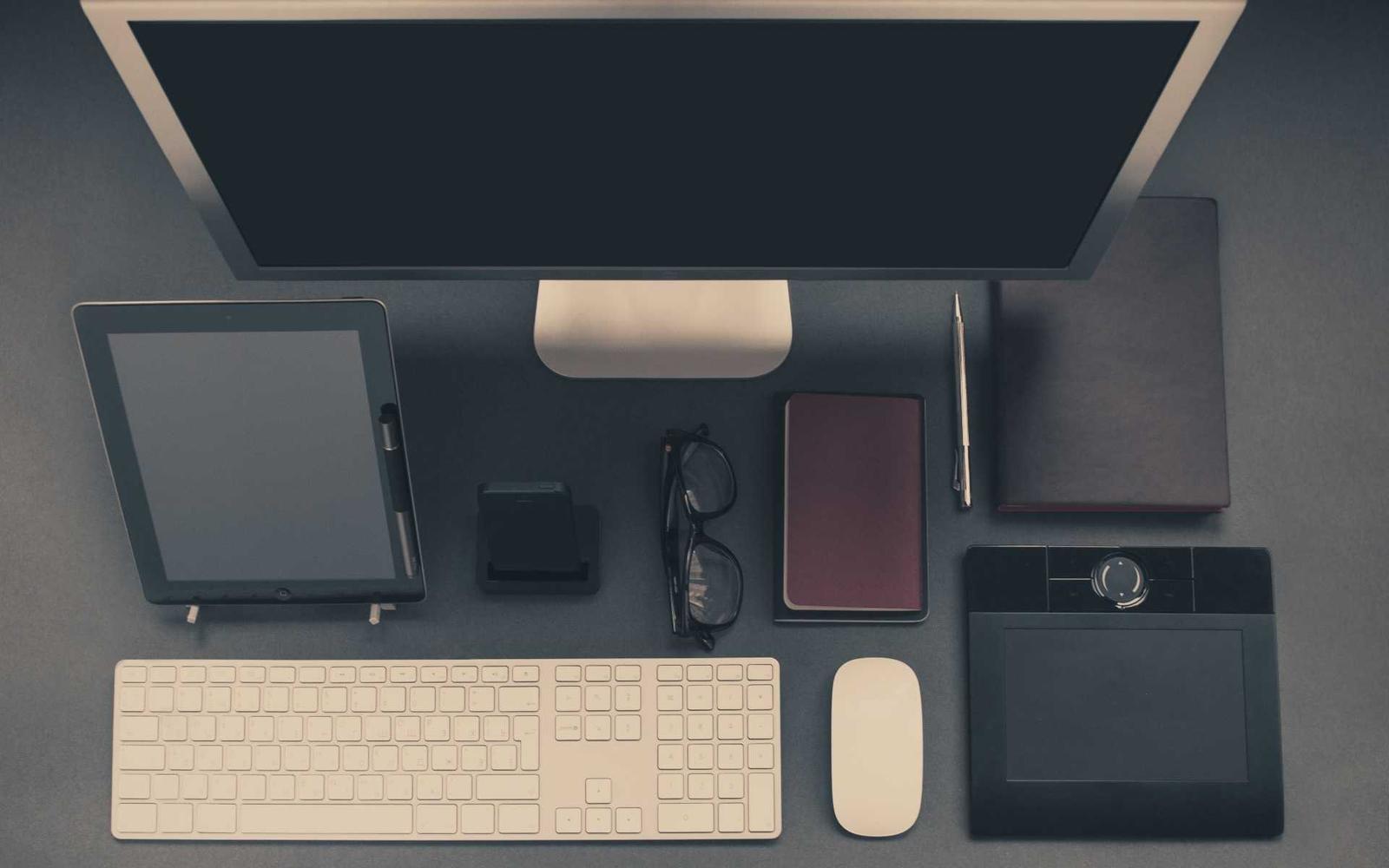 Un bureau vu du dessus : écran, clavier, tablette et carnets